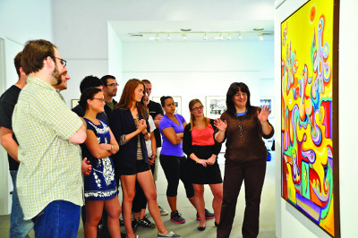 A group of people looking at a piece of art hanging on the wall. 