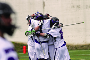 Group of male lacrosse players huddled up in uniform on the field